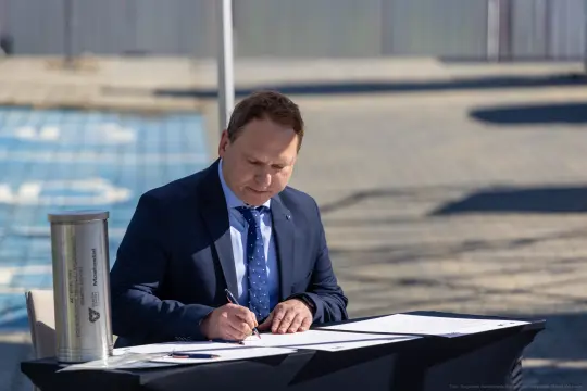 Mężczyzna w garniturze podpisuje dokumenty przy stole.