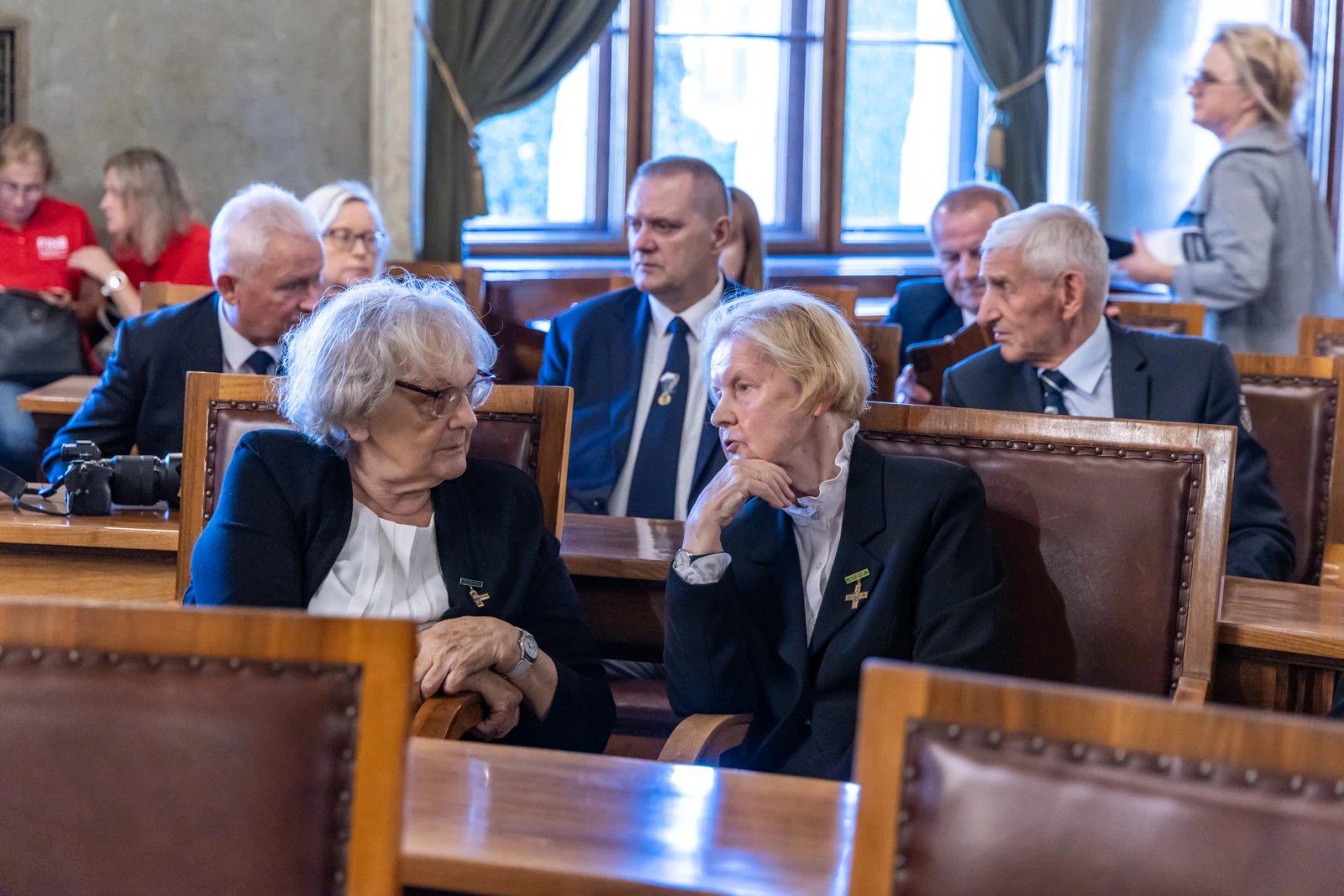 Dwie kobiety rozmawiają w sali pełnej osób w formalnych strojach.  Autor: Jan Graczyński