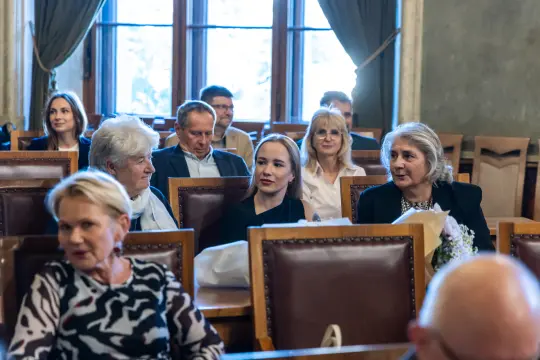 Grupa osób siedzących w sali, rozmawiających i uczestniczących w wydarzeniu.