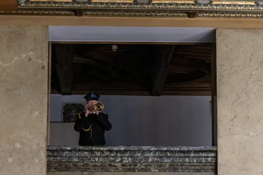 Mężczyzna w mundurze gra na trąbce z balkonu.