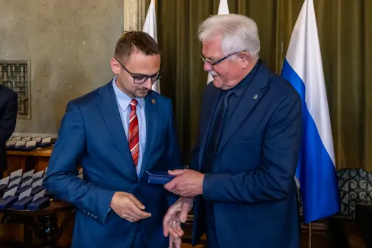 Wręczenie odznaczenia przez mężczyznę w garniturze drugiemu w eleganckim stroju.