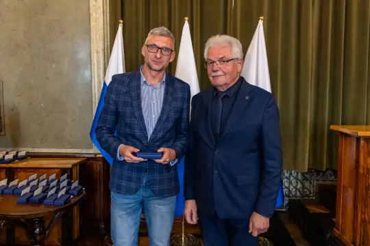 Mężczyzna w garniturze wręcza nagrodę drugiemu mężczyźnie w eleganckim stroju.
