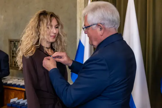 Wręczenie odznaczenia kobiecie przez mężczyznę w formalnym otoczeniu.