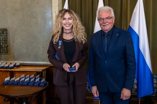 Wręczenie odznaczenia w uroczystej atmosferze, dwie osoby uśmiechnięte.