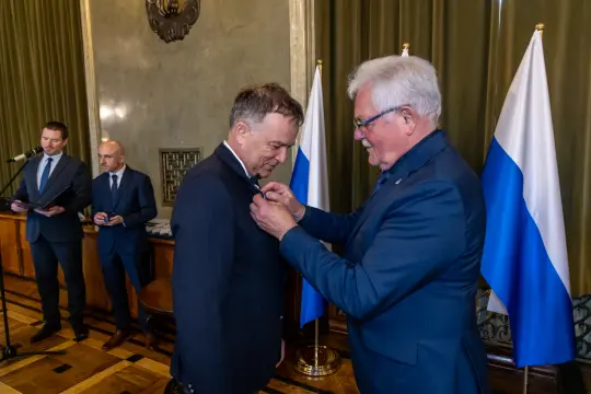 Uroczystość wręczenia odznaczenia w obecności flag rosyjskich.