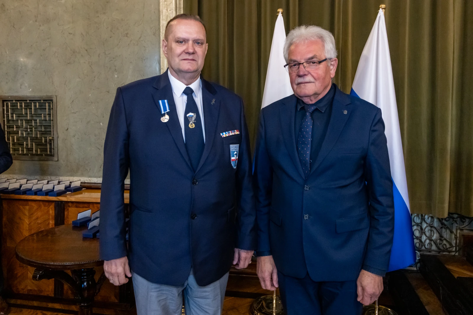 Dwaj mężczyźni w garniturach, jeden z medalami, stoją obok siebie w formalnym otoczeniu.  Autor: Jan Graczyński