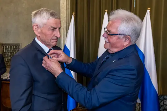 Mężczyzna odbiera odznaczenie od innego mężczyzny w formalnym otoczeniu.