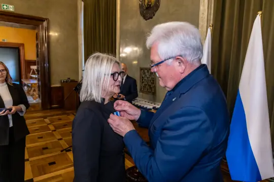 Wręczenie odznaczenia przez mężczyznę kobiecie w eleganckim otoczeniu.