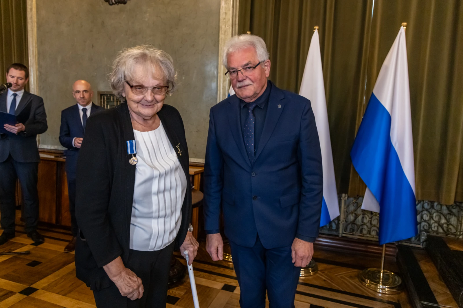 Wręczenie odznaczenia w uroczystej atmosferze, dwie osoby w formalnych strojach.  Autor: Jan Graczyński