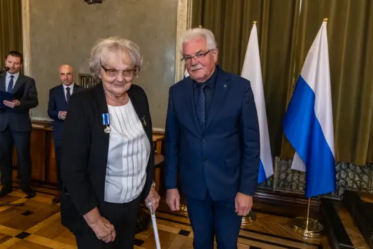 Wręczenie odznaczenia w uroczystej atmosferze, dwie osoby w formalnych strojach.