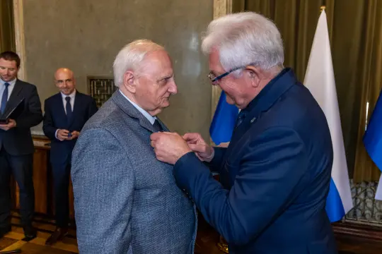Ceremonia wręczenia odznaczenia dwóm mężczyznom w formalnych strojach.