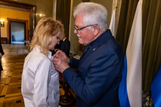 Wręczenie odznaczenia przez mężczyznę kobiecie w eleganckim wnętrzu.