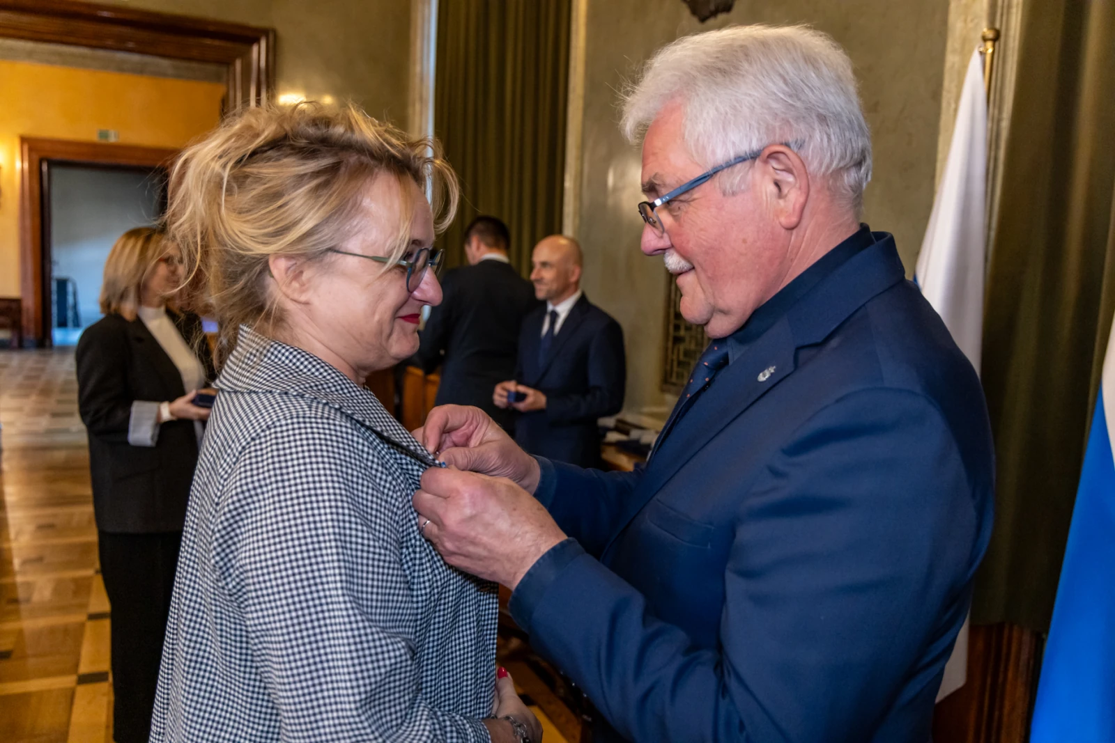 Wręczenie odznaczenia przez mężczyznę kobiecie w eleganckim wnętrzu.  Autor: Jan Graczyński