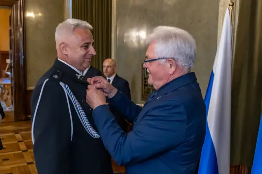 Uroczystość wręczenia odznaczenia mężczyźnie w mundurze policyjnym.
