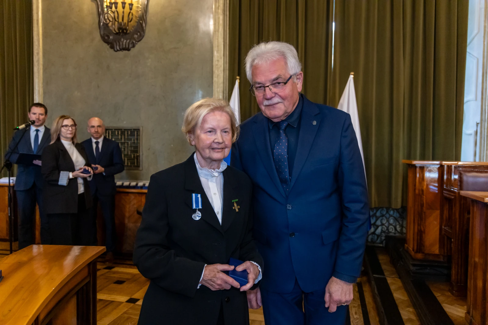 Uroczystość wręczenia odznaczeń, kobieta z medalem i mężczyzna w garniturze.  Autor: Jan Graczyński
