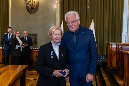 Uroczystość wręczenia odznaczeń, kobieta z medalem i mężczyzna w garniturze.