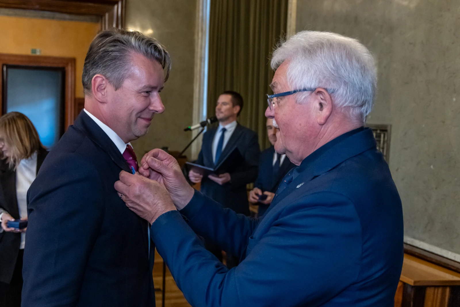 Ceremonia wręczenia odznaczenia mężczyźnie w garniturze.  Autor: Jan Graczyński