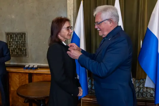 Wręczenie odznaczenia przez mężczyznę kobiecie w formalnym otoczeniu.
