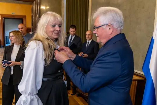 Wręczenie odznaczenia kobiecie przez mężczyznę w formalnym otoczeniu.