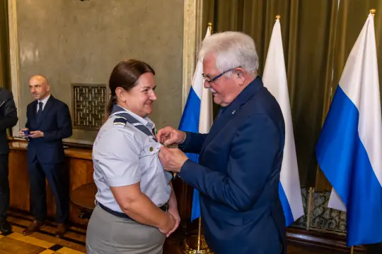 Wręczenie odznaczenia kobiecie w mundurze wojskowym przez mężczyznę w garniturze.