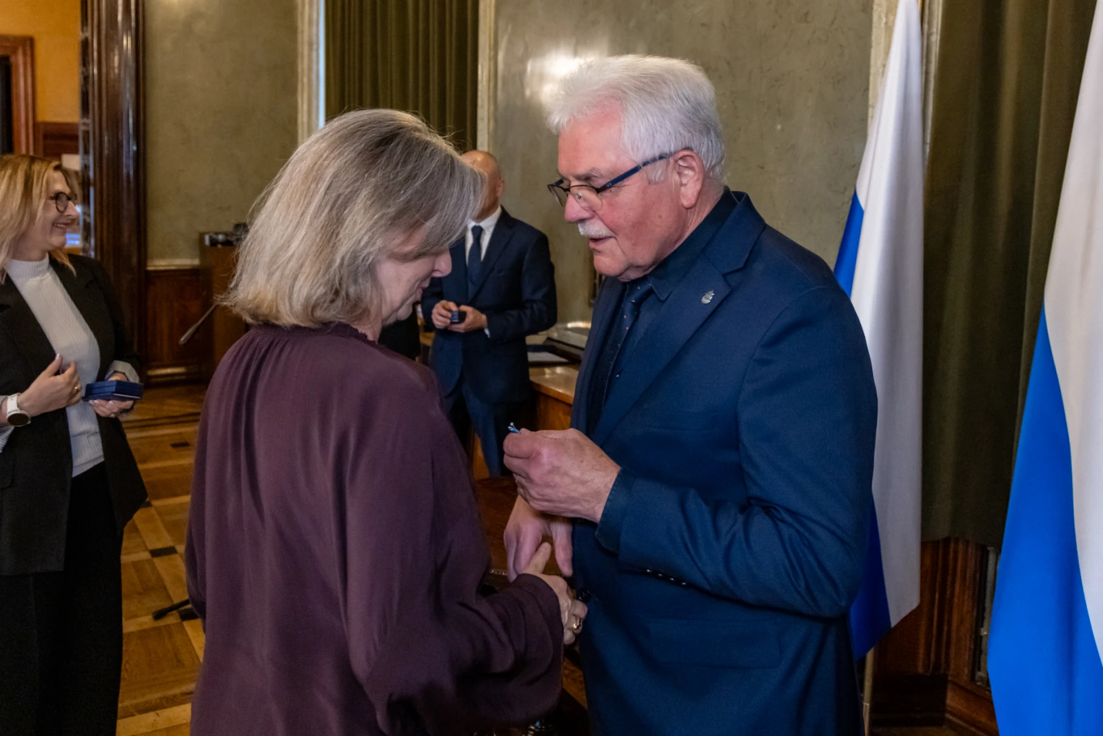 Wręczenie odznaczenia w formalnym otoczeniu, rozmowa dwóch osób.  Autor: Jan Graczyński