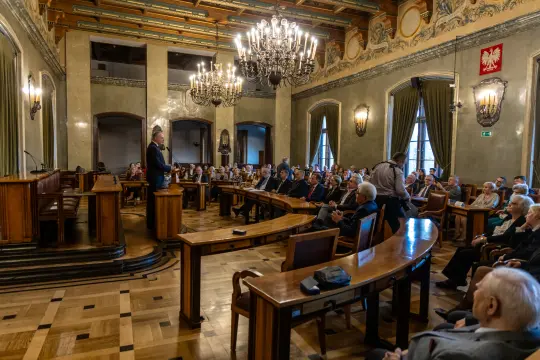 Spotkanie w eleganckiej sali z uczestnikami siedzącymi w rzędach.