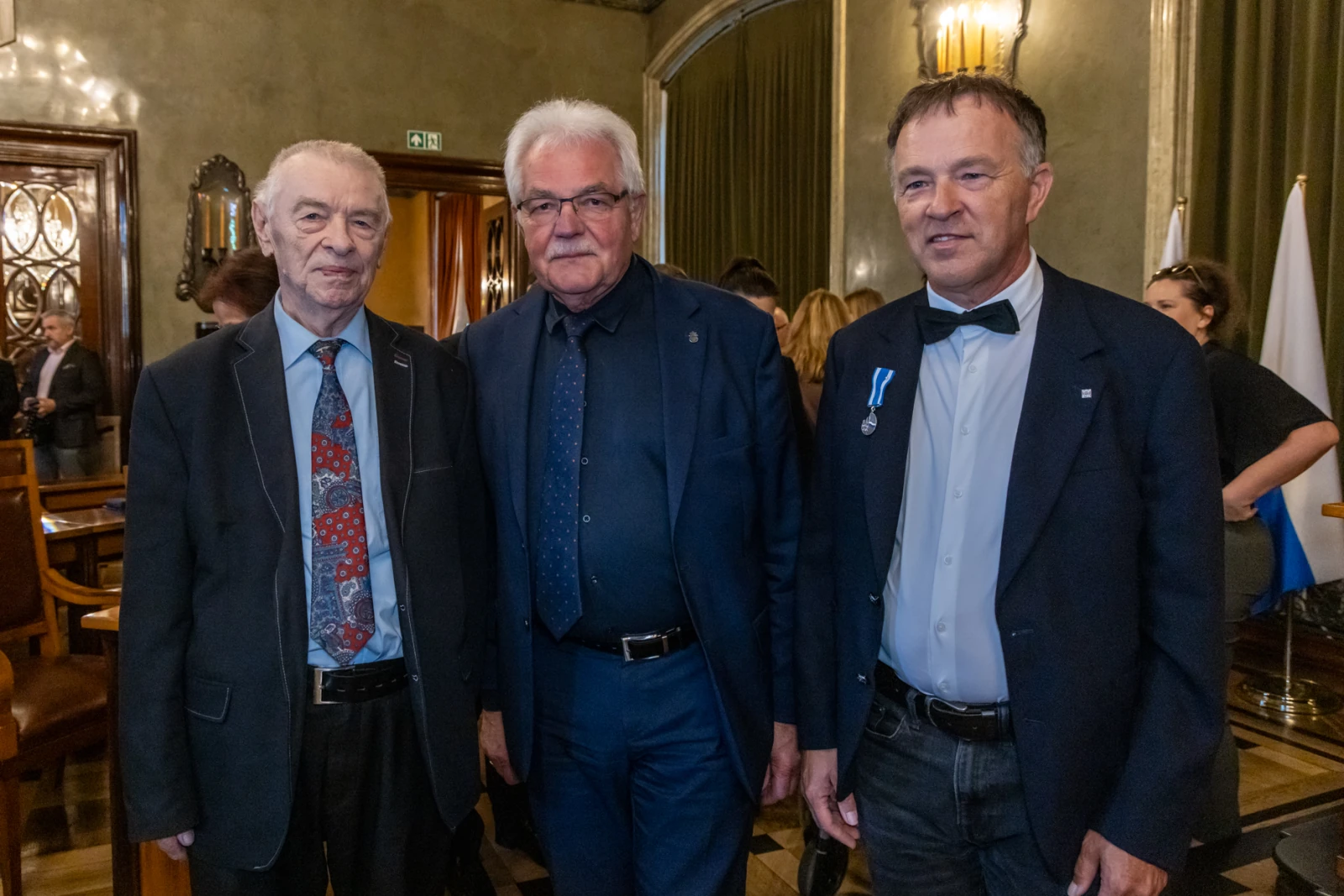 Trzech mężczyzn w eleganckich strojach, stojących obok siebie w stylowym wnętrzu.  Autor: Jan Graczyński