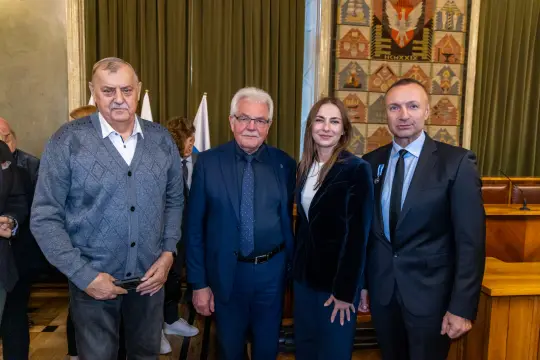 Cztery osoby w formalnych strojach stoją obok siebie w sali z dekoracjami.