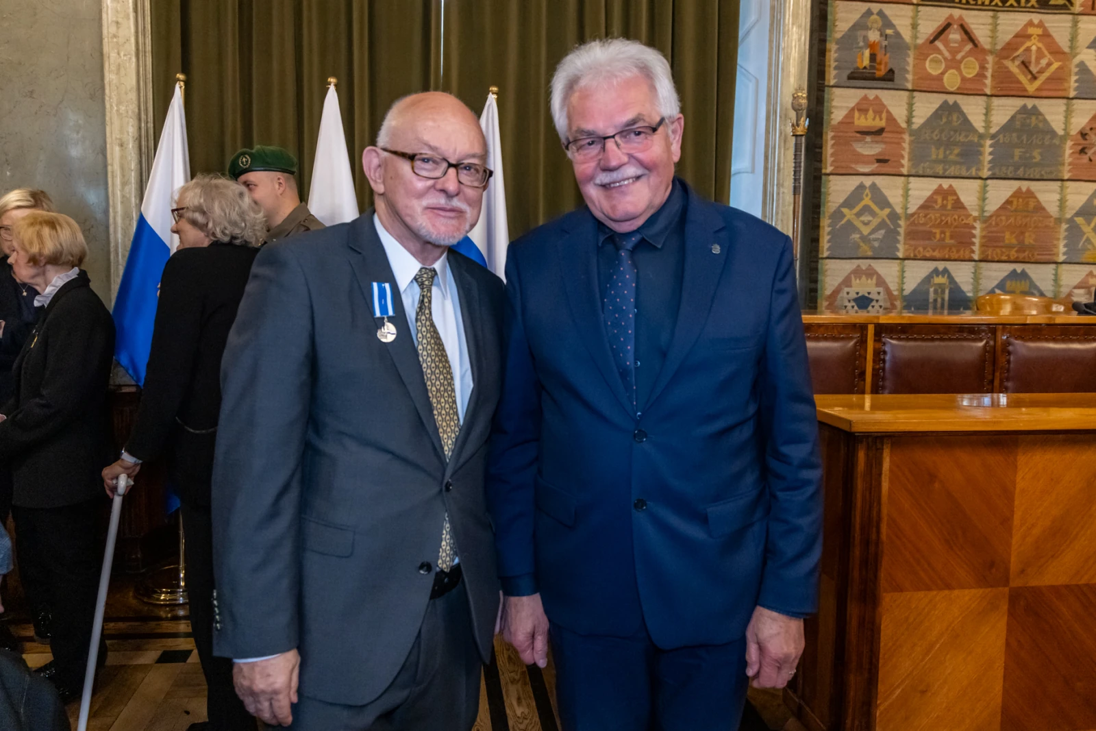 Dwaj mężczyźni w garniturach, uśmiechnięci, stoją obok siebie w eleganckim wnętrzu.  Autor: Jan Graczyński