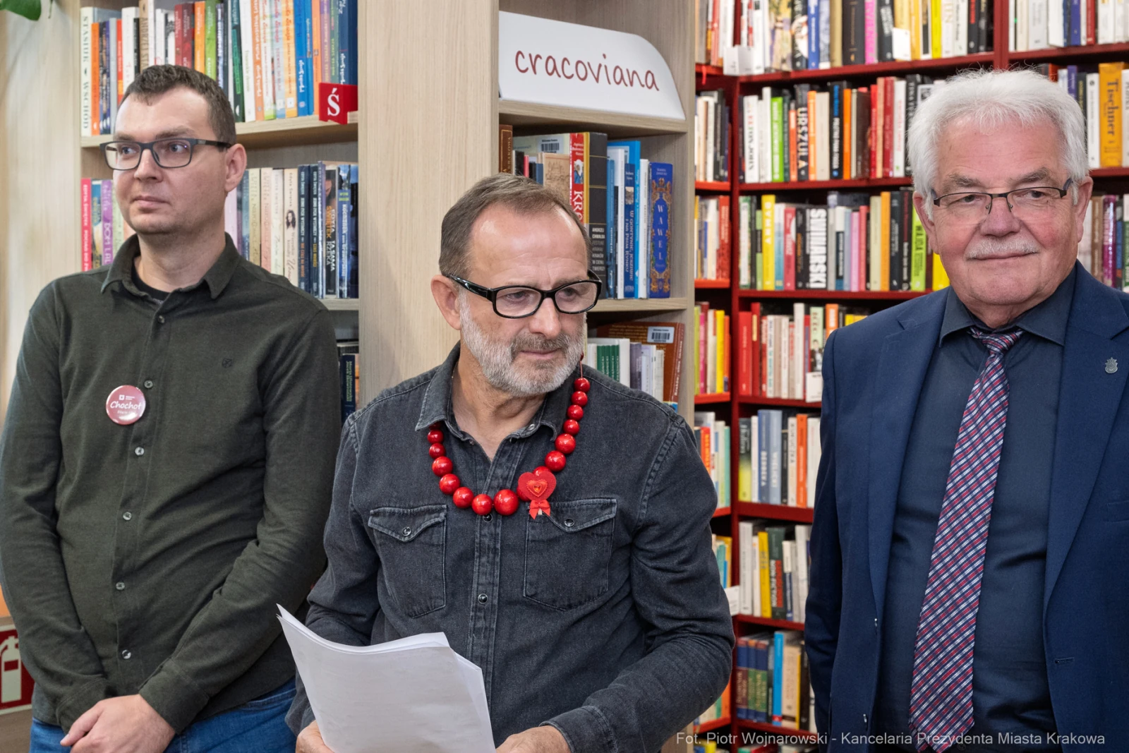 Trzech mężczyzn w bibliotece, jeden z naszyjnikiem, wszyscy w formalnych strojach.  Autor: Piotr Wojnarowski
