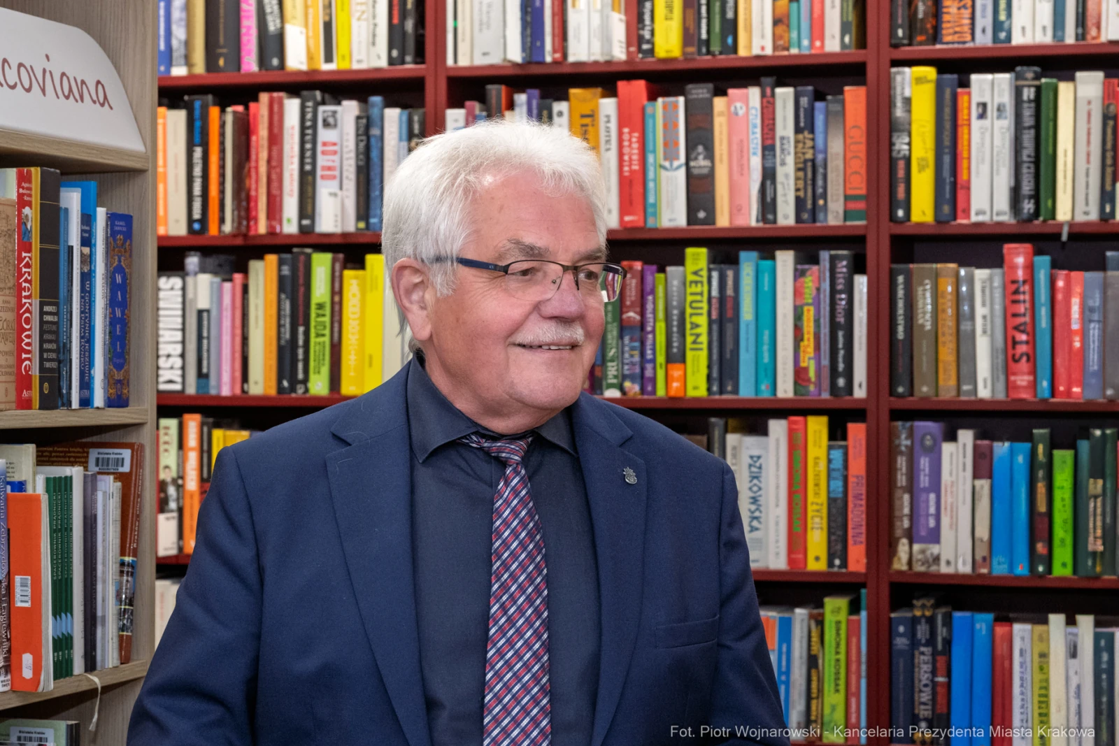 Mężczyzna w okularach, uśmiechający się, stoi przed półką z książkami.  Autor: Piotr Wojnarowski