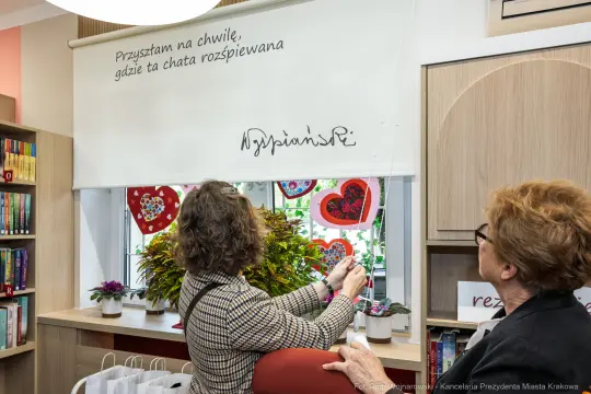 Kobieta odsłania zasłonę z napisem i sercami w bibliotece.