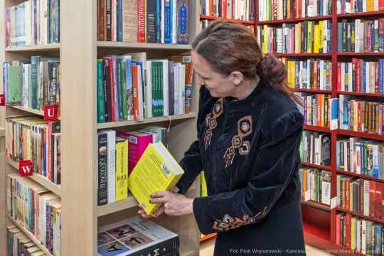 Kobieta przegląda książki na półce w bibliotece.