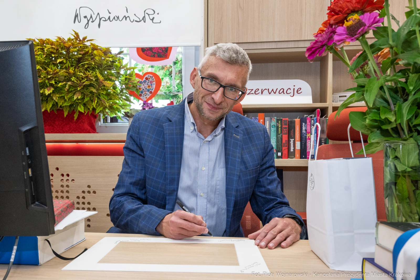 Mężczyzna piszący w biurze, otoczony książkami i kwiatami.  Autor: Piotr Wojnarowski