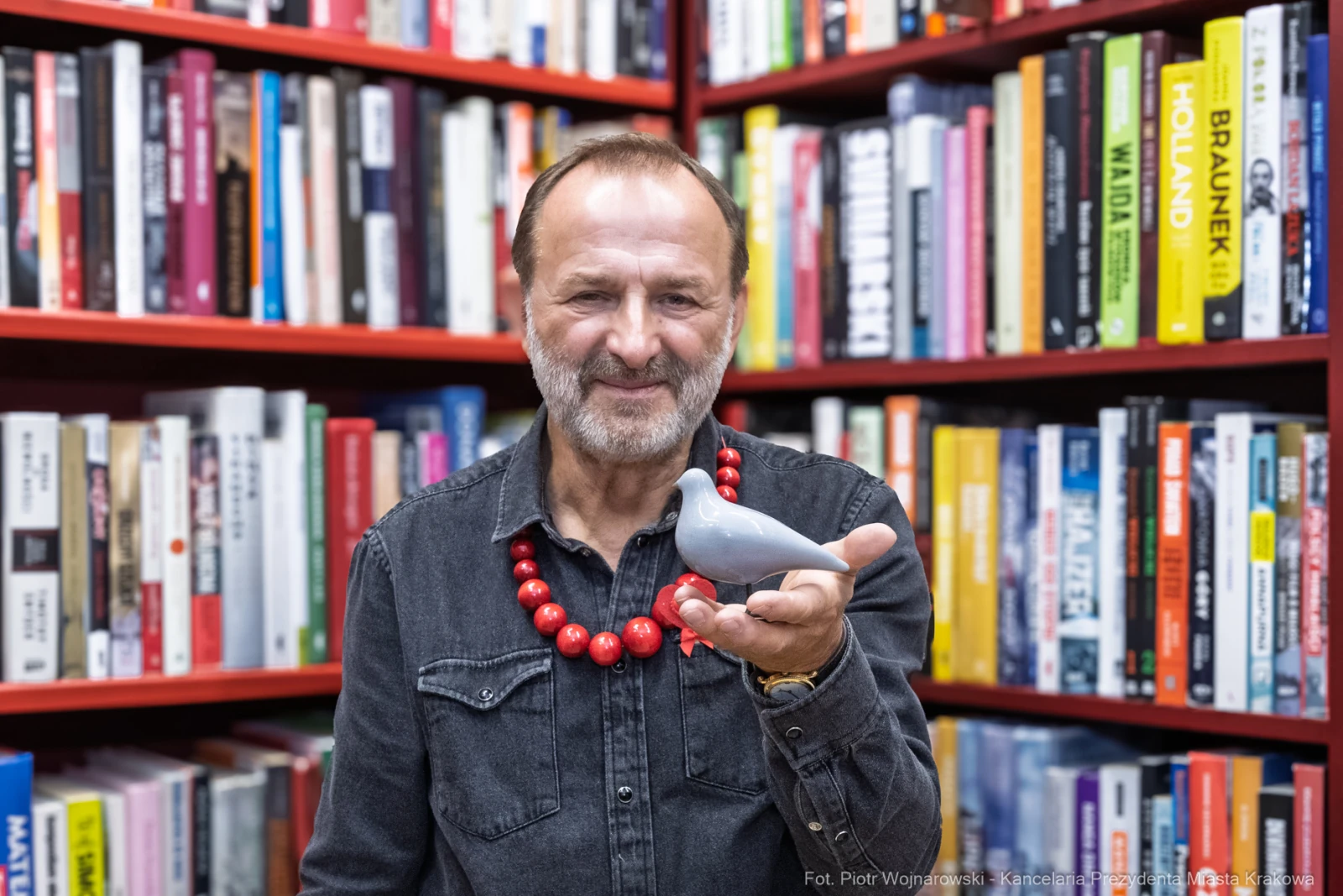 Mężczyzna z brodą trzyma w dłoni szarego ptaka, w tle regał z książkami.  Autor: Piotr Wojnarowski