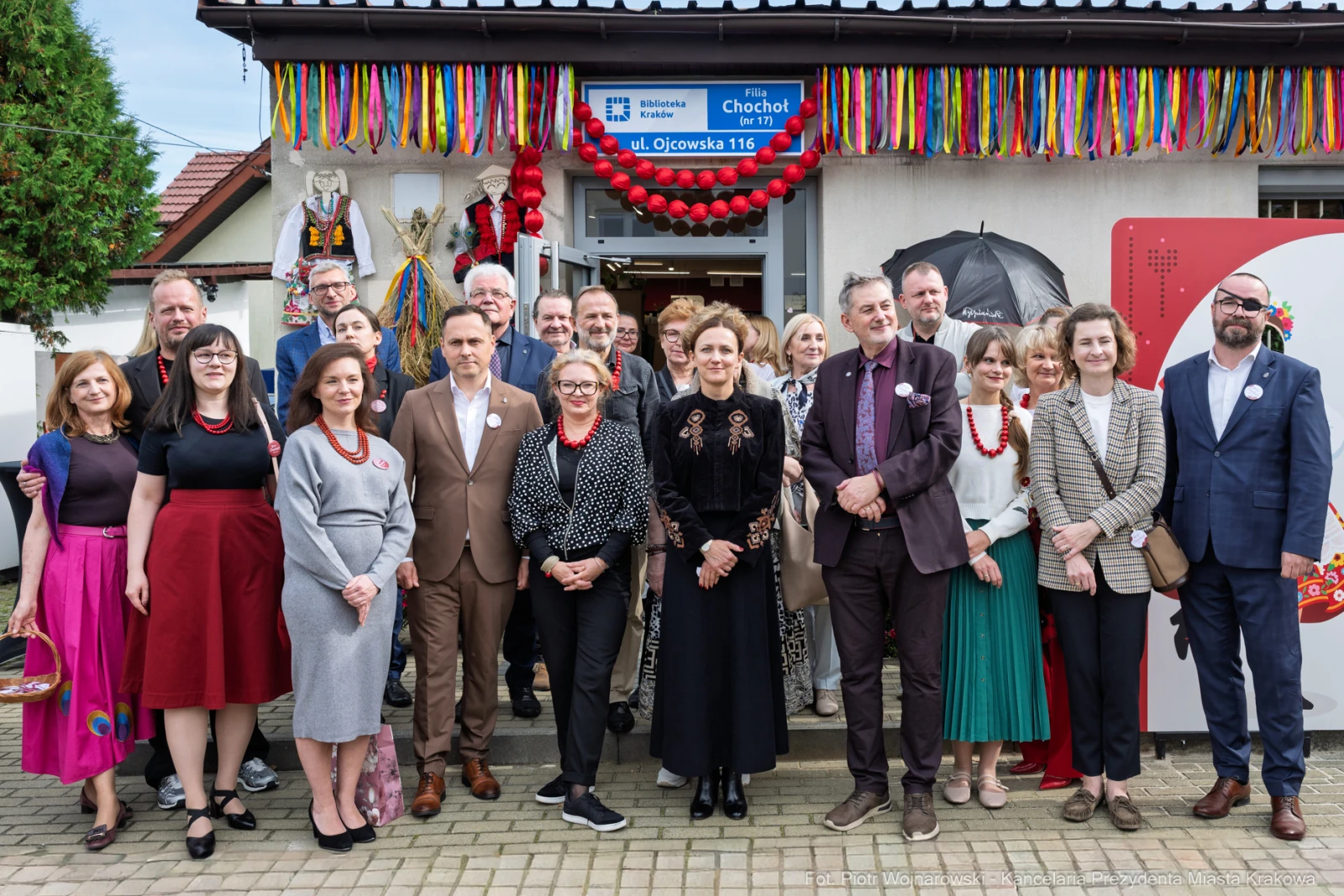Grupa ludzi w strojach formalnych przed budynkiem, udekorowanym kolorowymi ozdobami.  Autor: Piotr Wojnarowski