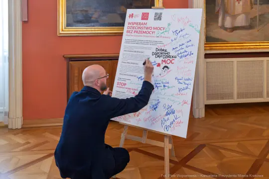 Mężczyzna podpisuje plakat promujący wsparcie dla dzieci i walkę z przemocą.