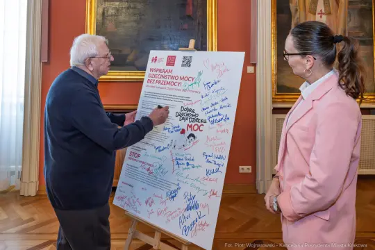 Mężczyzna podpisuje plakat promujący wsparcie dla ofiar przemocy, obok stoi kobieta.