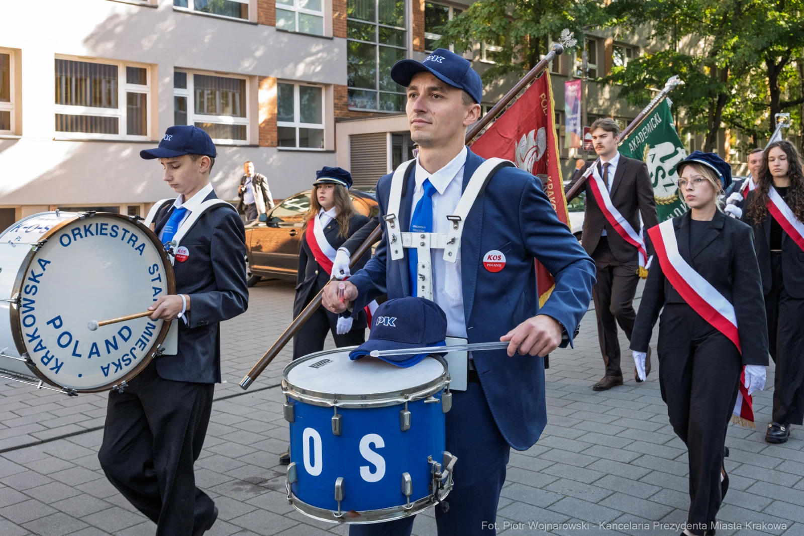 Mężczyzna w garniturze gra na bębnie, towarzyszą mu członkowie orkiestry i sztandary.  Autor: Piotr Wojnarowski