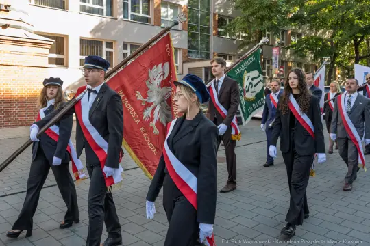 Uczestnicy parady z flagami i sztandarami, ubrani w eleganckie stroje.