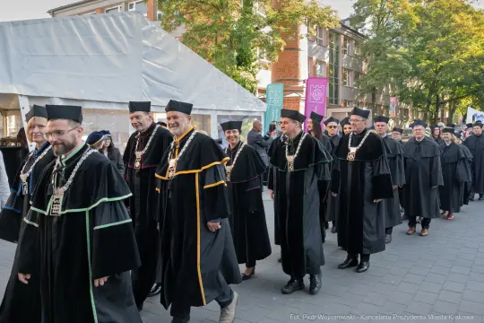 Uczestnicy parady w akademickich togach, idący ulicą w Krakowie.
