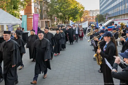 Uczestnicy parady w akademickich togach, z orkiestrą i transparentami.