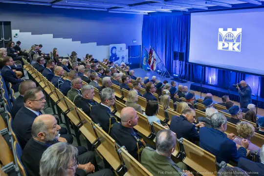 Zgromadzenie osób w sali konferencyjnej, na podium logo PK.
