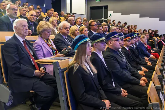 Grupa ludzi w formalnych strojach siedząca na widowni podczas wydarzenia.