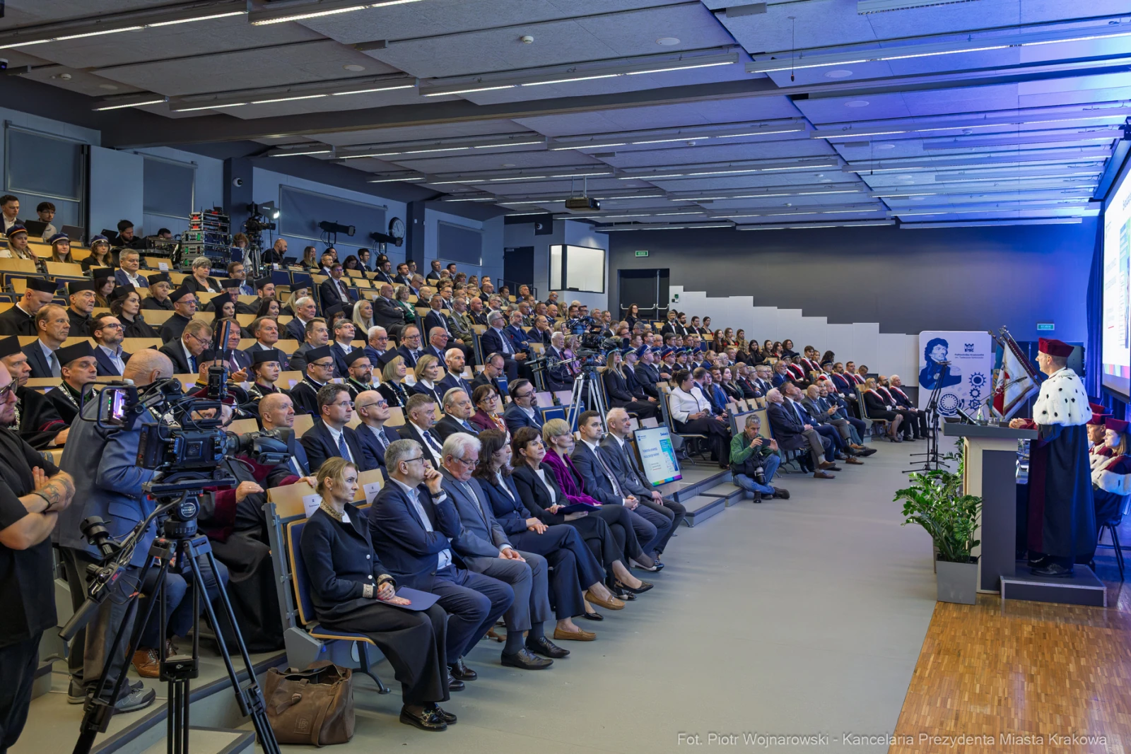 Konferencja z dużą liczbą uczestników, prelegent na scenie, kamery i sprzęt nagrywający.  Autor: Piotr Wojnarowski