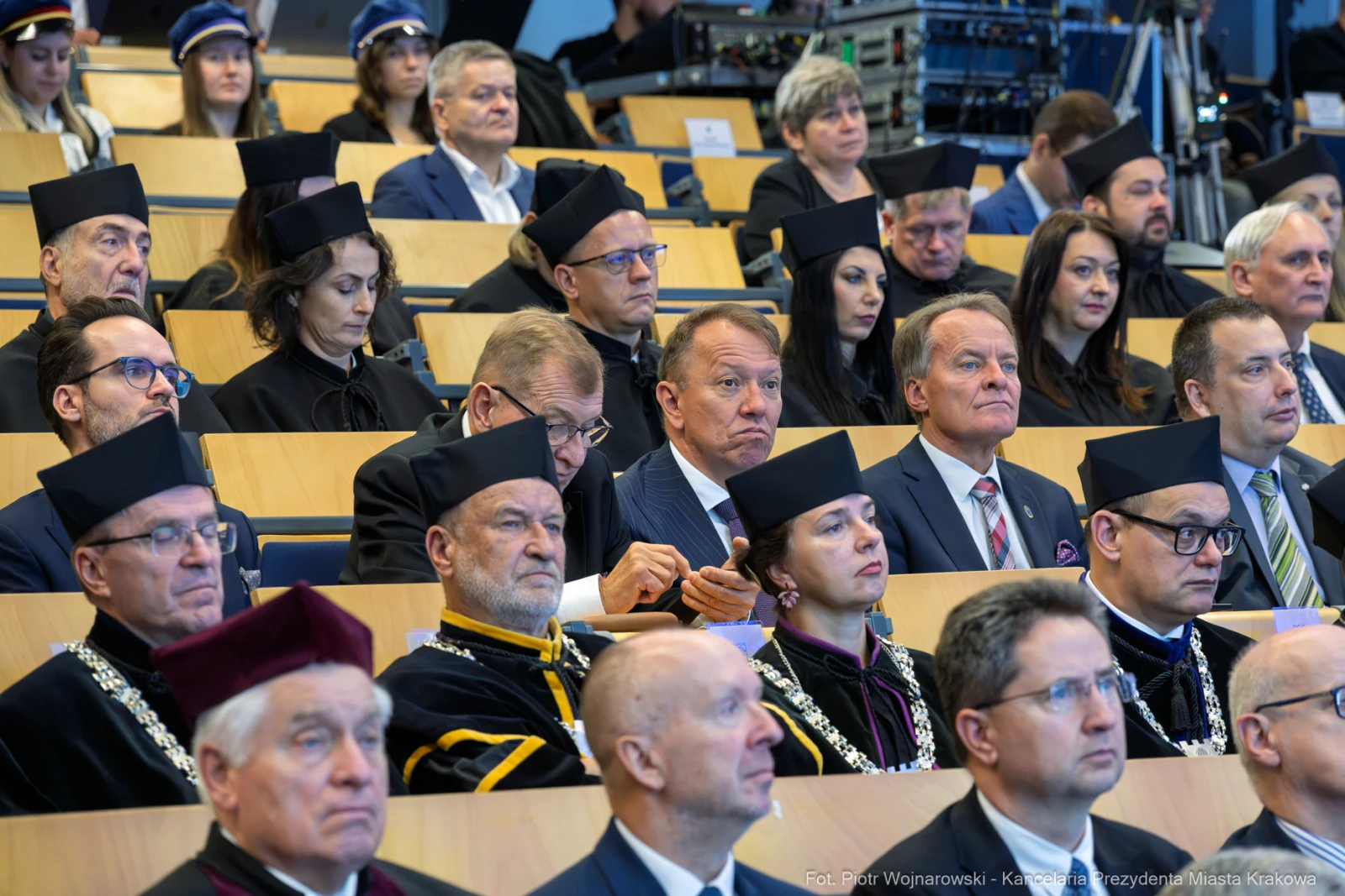 Grupa ludzi w akademickich togach siedzących na widowni podczas uroczystości.  Autor: Piotr Wojnarowski