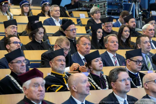 Grupa ludzi w akademickich togach siedzących na widowni podczas uroczystości.