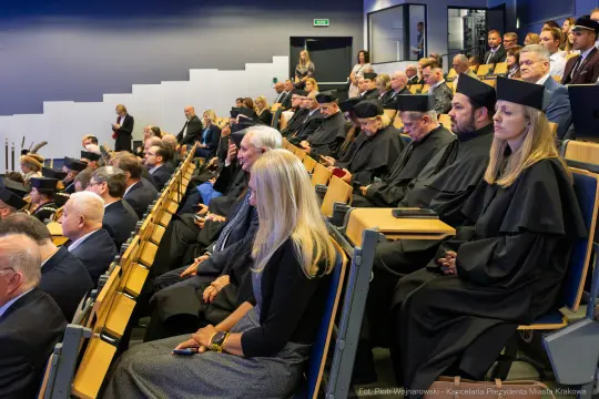 Uczestnicy ceremonii w togach akademickich siedzą na widowni.