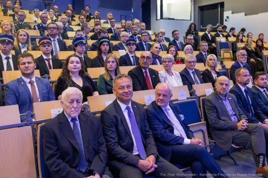 Grupa ludzi siedzących na widowni podczas wydarzenia, w tym mężczyźni w garniturach i kobiety w eleganckich strojach.