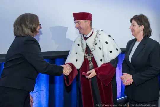 Uroczystość wręczenia nagrody z udziałem mężczyzny w togach i dwóch kobiet.